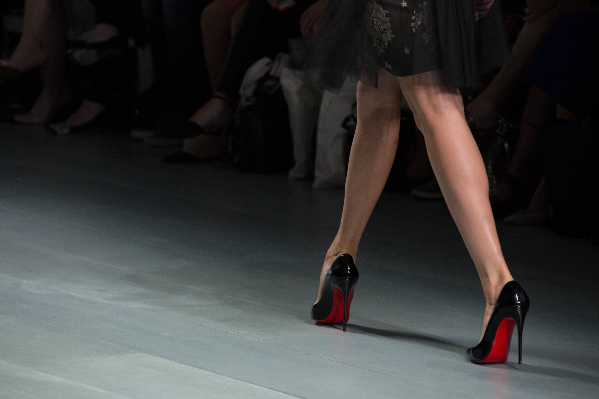 Woman walking the runway in black Louboutin heels with red soles.