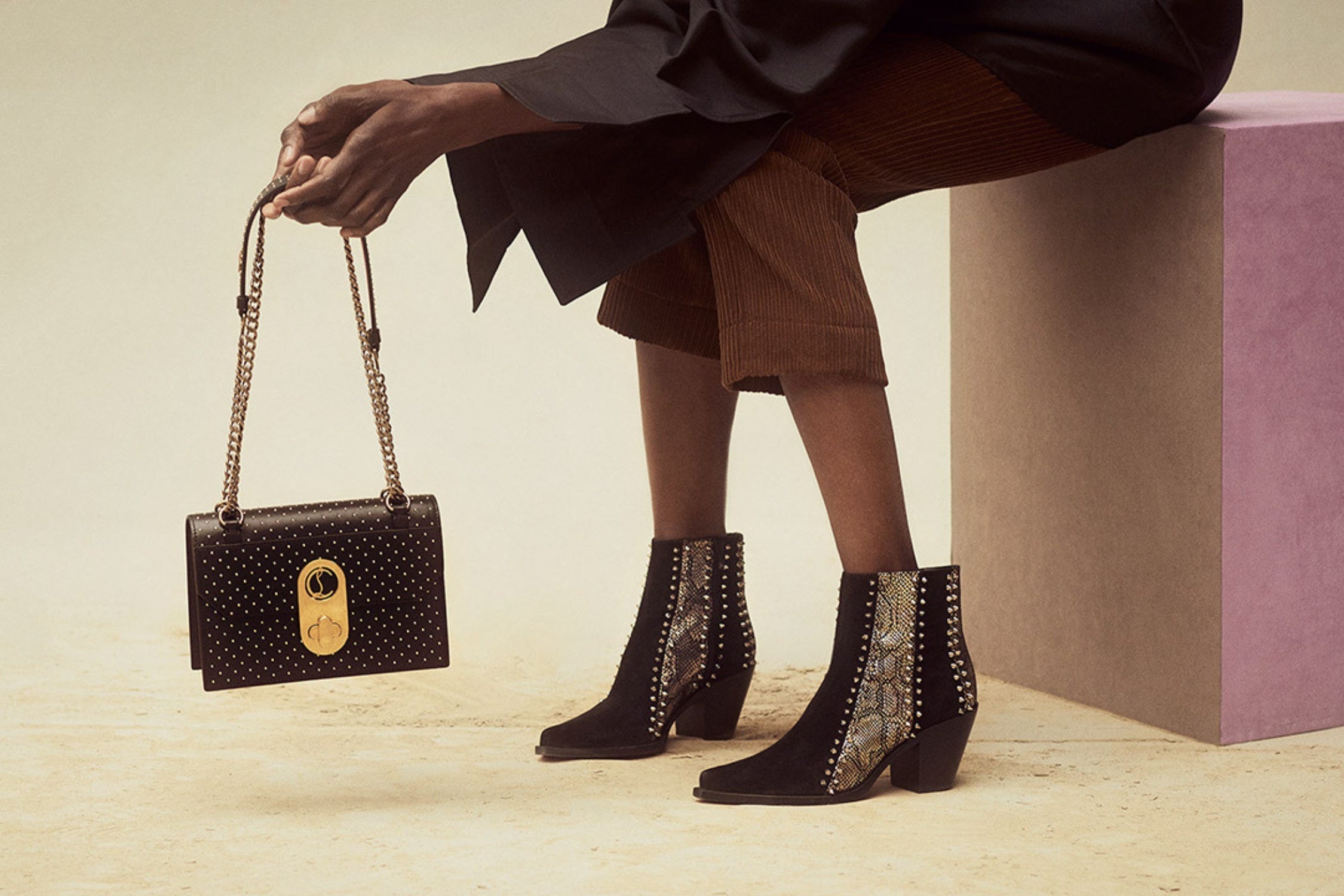 Close-up of a woman wearing studded black ankle boots with snakeskin panels, holding a black designer handbag.