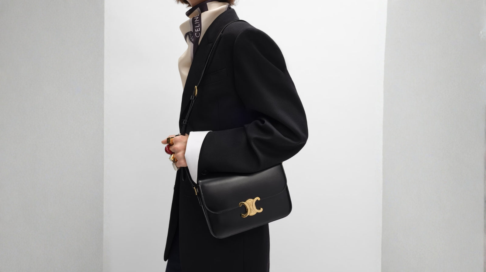 Model styling a black Celine Triomphe bag with a tailored blazer and silk scarf.