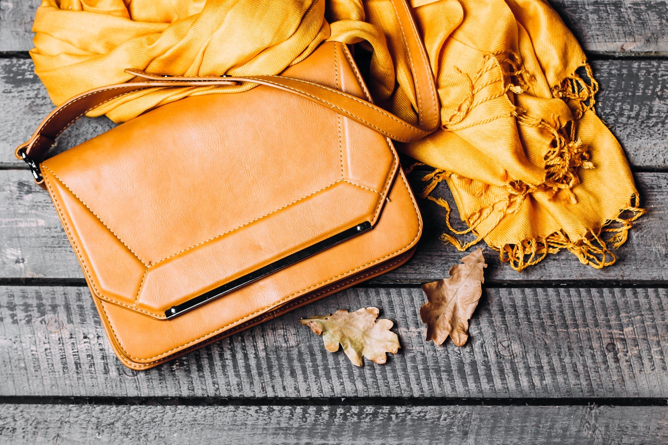 Tan leather designer handbag styled with a yellow scarf on wooden background.