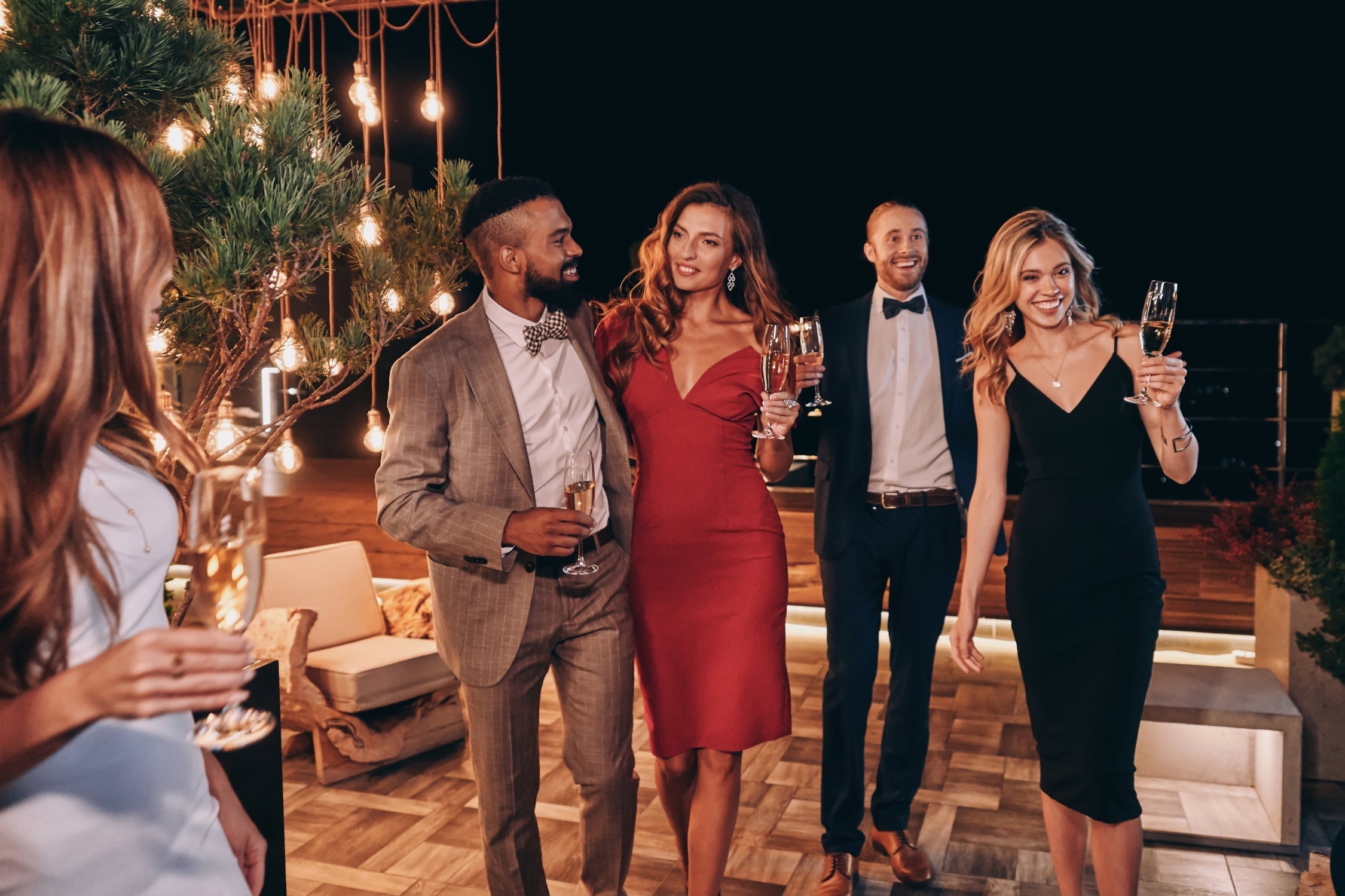 Guests dressed in elegant outfits celebrating an evening fall wedding with champagne under warm string lights.