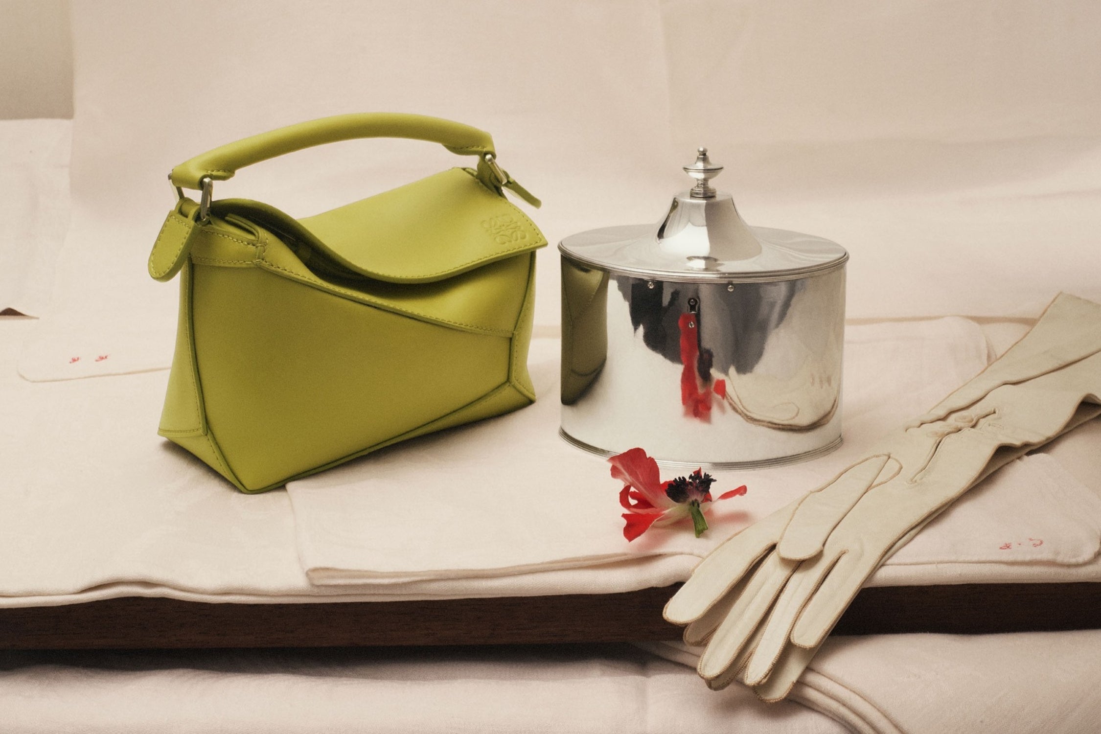 Lime green luxury handbag displayed beside silver decor and cream gloves on fabric surface.