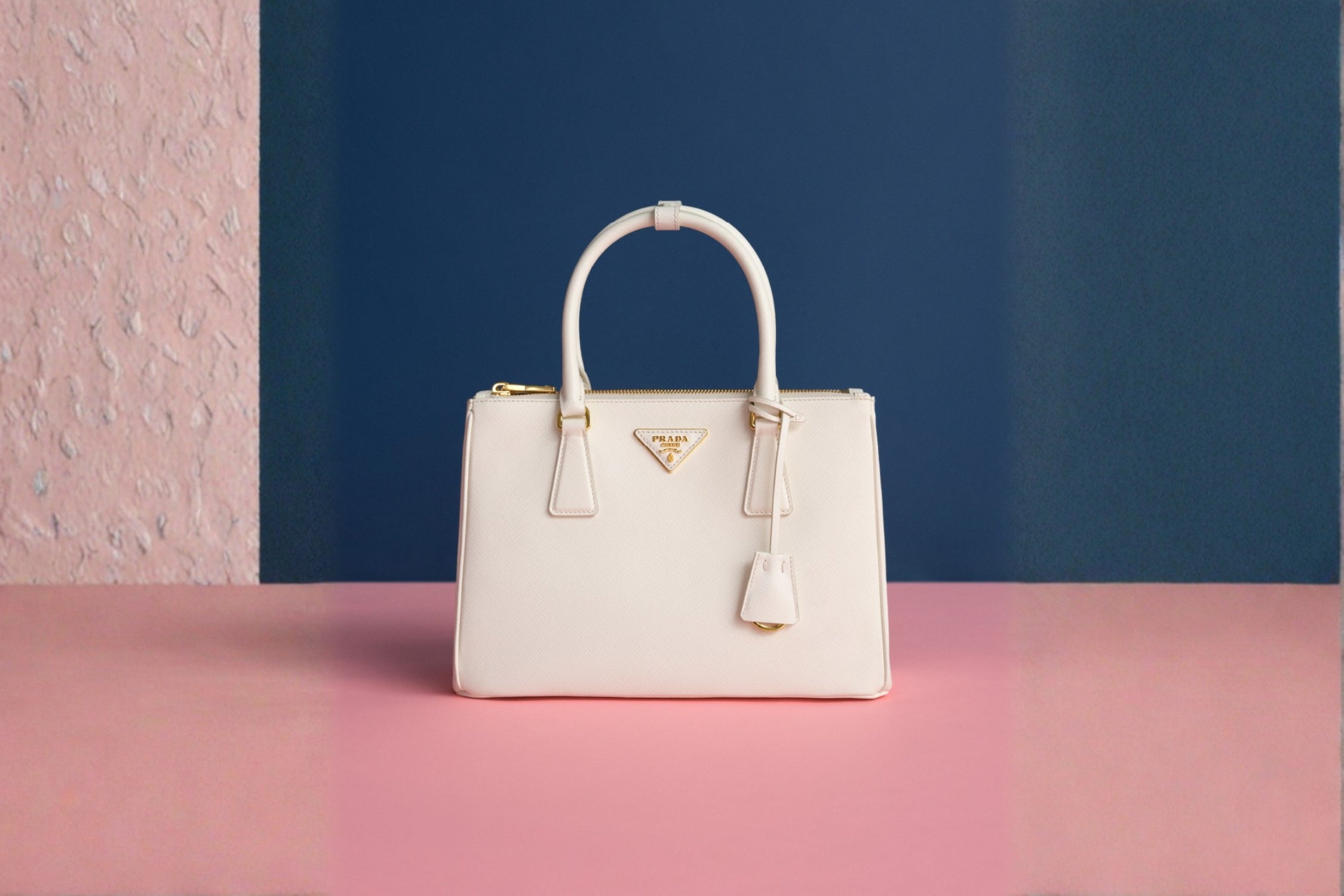 Close-up of a white Prada Galleria bag with gold accents, displayed on a pink and blue background.