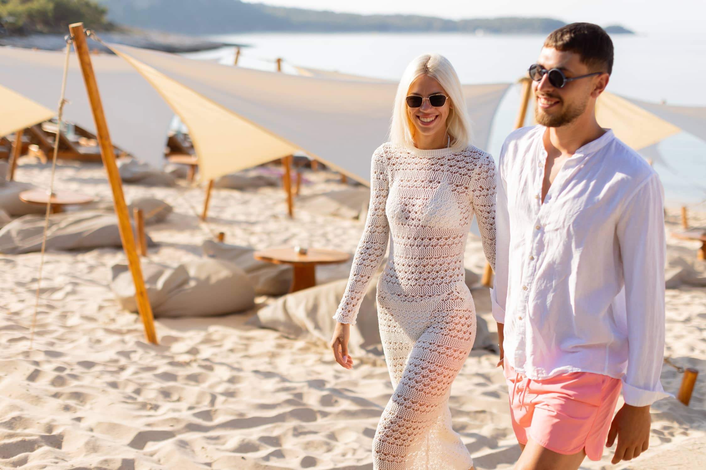 Couple walking on the beach in chic resort wear outfits.
