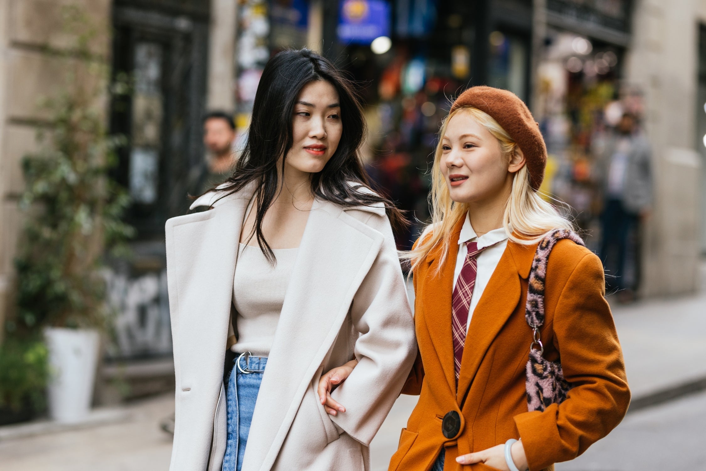 Two women in chic coats walking arm in arm, showcasing street style fashion.