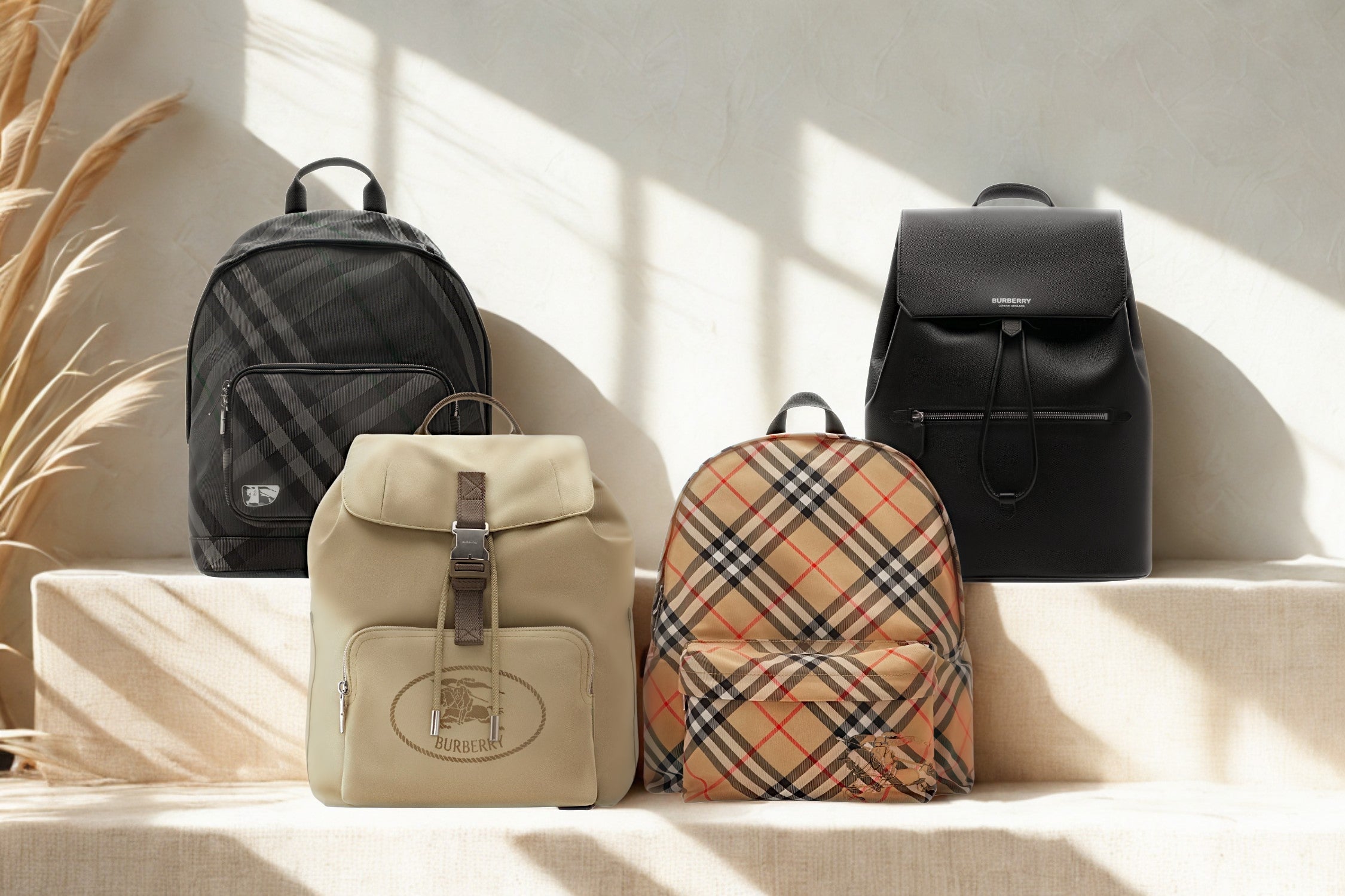 Four Burberry backpacks displayed on beige steps under natural sunlight.