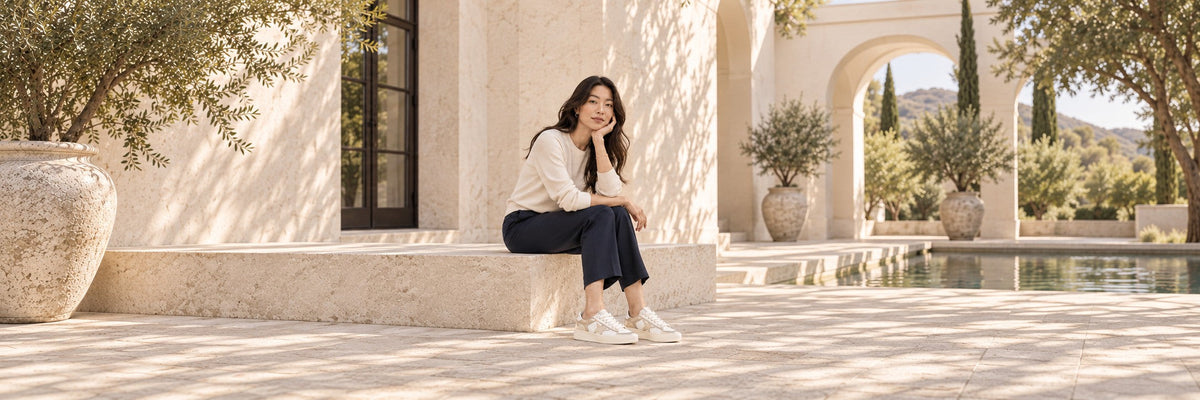 Editorial styling illustration of a woman wearing white-and-gold Golden Goose star sneakers with navy trousers.